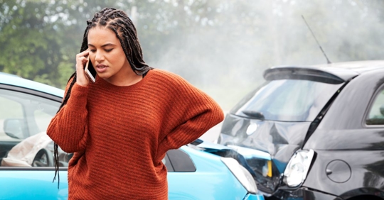 Woman on the phone in front of two crashed vehicles